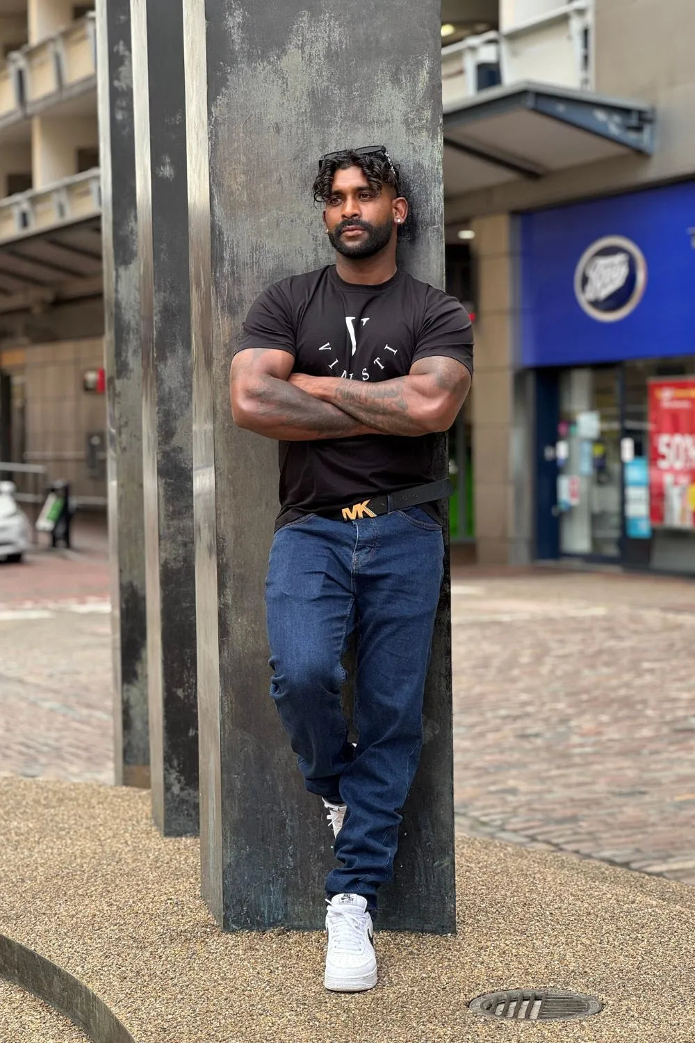 Man standing between two concrete pillars with a building and store in the background
