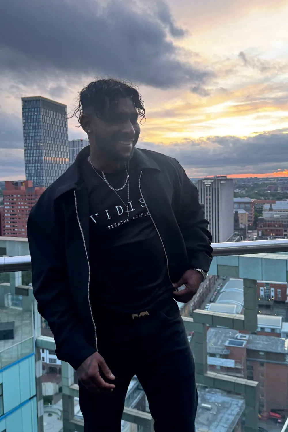 Person standing on a balcony with a cityscape and sunset in the background