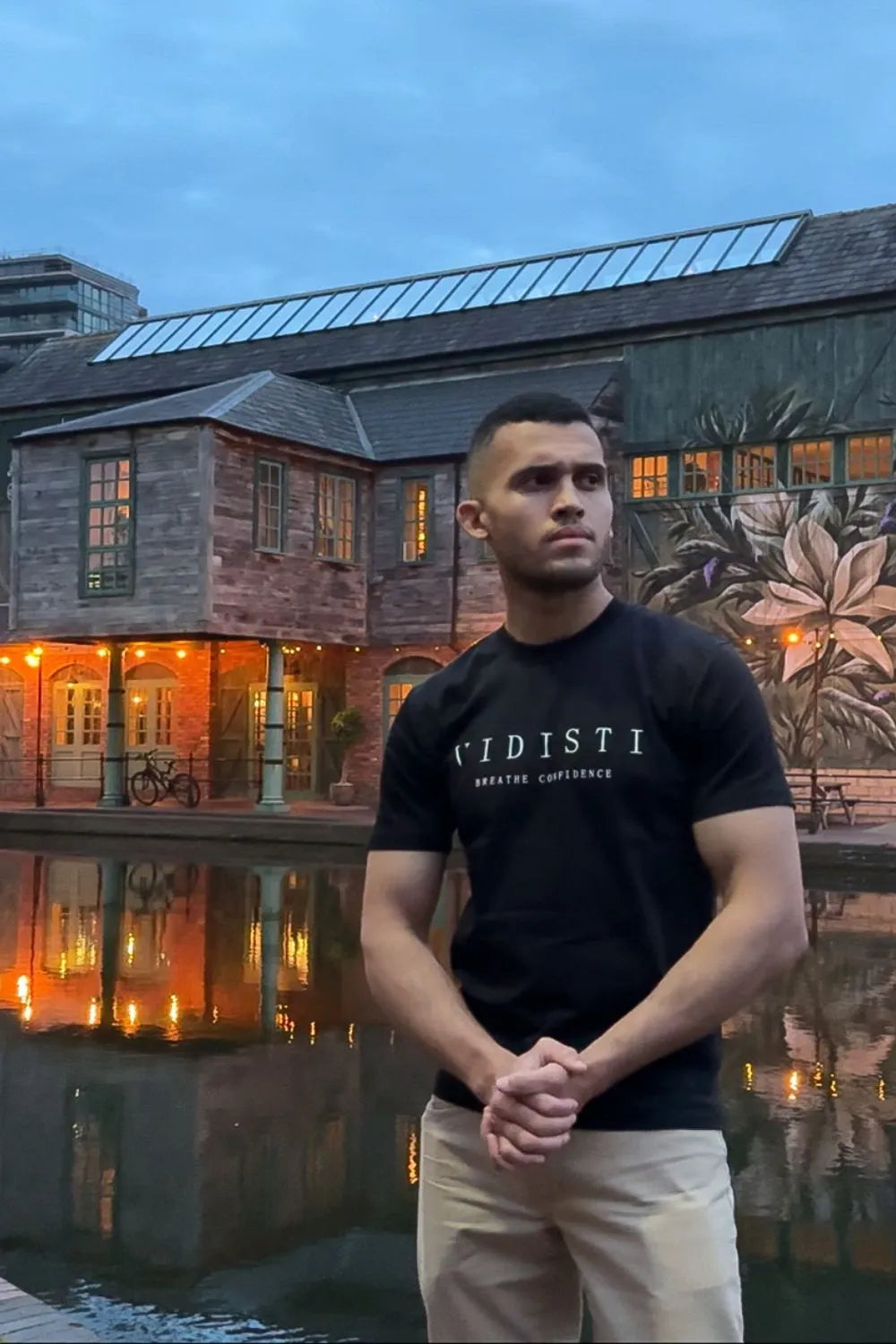 Man wearing a black t-shirt with 'VIDISTI' logo standing in front of a building with a mural.
