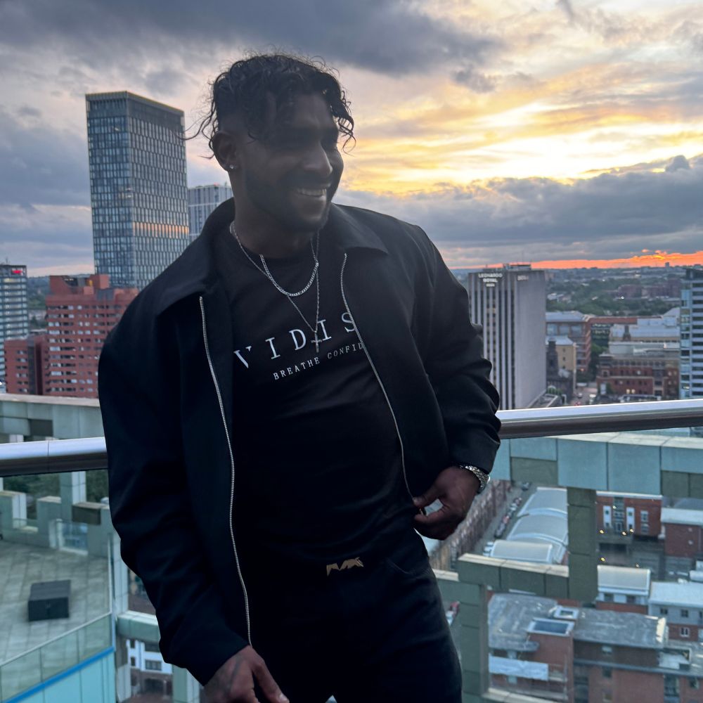 Person standing on a balcony with a cityscape and sunset in the background